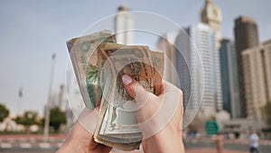 The girl counts in her hands the money of the United Arab Emirates against the background of the city center of Dubai.