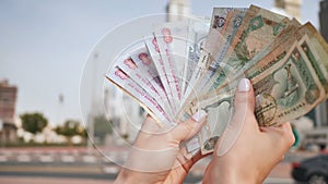 The girl counts in her hands the money of the United Arab Emirates against the background of the city center of Dubai.