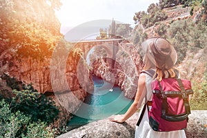 A girl in a cowboy hat with a backpack enjoys an incredibly beautiful view of a stone bridge over the gorge Fiordo di Furore.