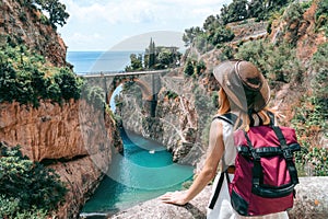 A girl in a cowboy hat with a backpack enjoys an incredibly beautiful view of a stone bridge over the gorge Fiordo di Furore. photo