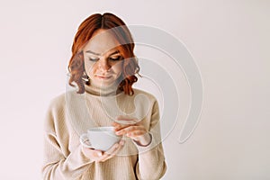 Girl in a cozy sweater, holding a mug with coffee on white background.