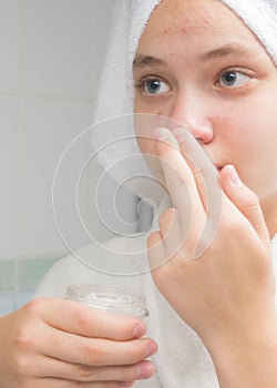 Girl with cream in hand stands in front of a mirror in the bathroom