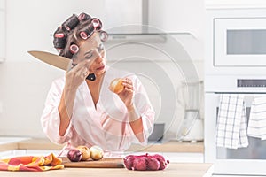 Girl cries over onion chopping in the kitchen wearing head curlers in the kitchen