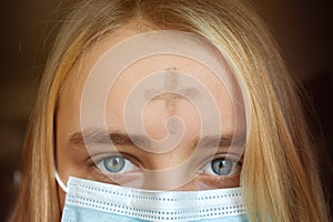 Girl with cross made from ash on forehead with face mask. Ash wednesday concept.