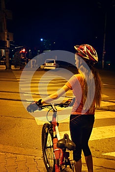 Girl is crossing zebra crosswalk on bicycle at night city.