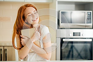 Girl cuddling a tablet and looking above on a white wall