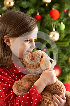 Girl Cuddling Teddy In Front Of Christmas Tree