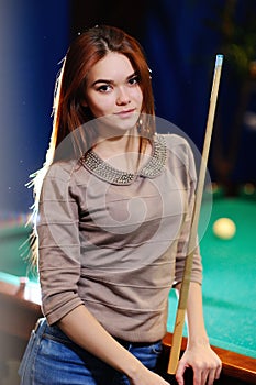 Girl with a cue in her hands playing billiards