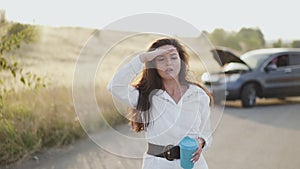 Girl with cup in hand corrects hair, talks and looks around at broken car