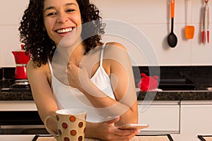 Girl with curly hair holding cell phone and laughing in the kitchen