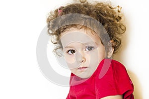 Girl with curly hair and long eyelashes. kid looks thoughtfully at the camera. baby in festive red clothes. human emotions