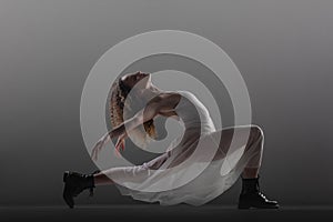 Girl with curly hair making ballet poses. Ballerina in white dress and black boots