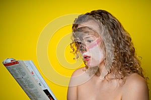 A girl with a curly hair, reads the newspaper in surprise