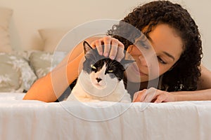 Girl with curly hair smiling at domestic cat pet in bed. Concept of love to animals, pets, lifestyle, care, tranquility, peace,