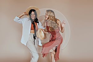 Girl with curly shiny hair dancing on brown background. Indoor photo of two ladies in canotier..