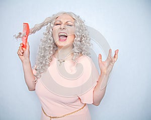 Girl with curly white hair can`t comb her loose dry hair and is upset about it. a blonde woman stands in a pink dress with an oran