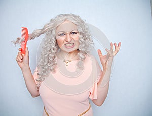 Girl with curly white hair can`t comb her loose dry hair and is upset about it. a blonde woman stands in a pink dress with an oran