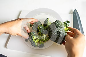 A girl cuts broccoli for soup. Sliced ??broccoli on a cutting board. A woman is preparing broccoli.