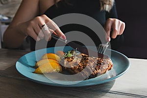 Girl cuts juicy grilled turkey steak with knife and fork.