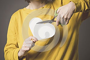 Girl cuts a paper white heart with scissors, hands closeup.