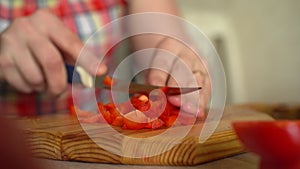 Girl cuts tomato for salad with a sharp knife. male chef prepares salad in the kitchen at home. Cooking a delicious