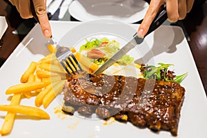 Girl cutting Roasted barbecue pork ribs, focus on sliced meat