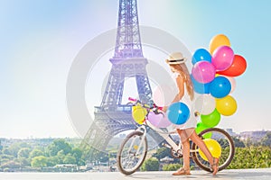 Girl cycling through Paris with colorful balloons