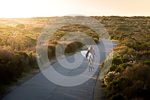 Beautiful blonde surfer girl on her way to the beach on her bicycle with her surfboard.