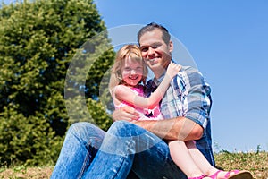 Girl on dads lap sitting on meadow or in field