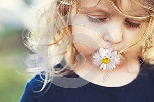 Girl with a daisy flower  on a green background close. lips with flower on  grass background. portrait of a little