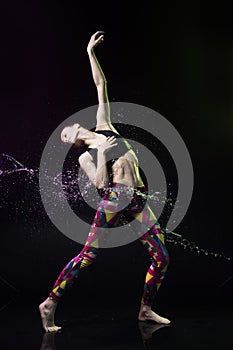 The girl dances on the floor covered with water on a black background and water splashes around her