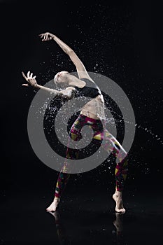 The girl dances on the floor covered with water on a black background and water splashes around her