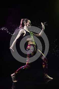 The girl dances on the floor covered with water on a black background and water splashes around her