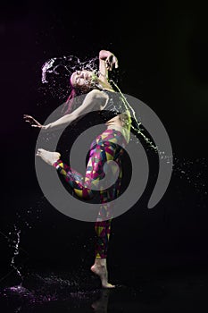 The girl dances on the floor covered with water on a black background and water splashes around her