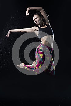 The girl dances on the floor covered with water on a black background and water splashes around her