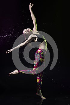 The girl dances on the floor covered with water on a black background and water splashes around her