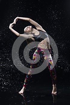 The girl dances on the floor covered with water on a black background and water splashes around her