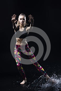 The girl dances on the floor covered with water on a black background and water splashes around her