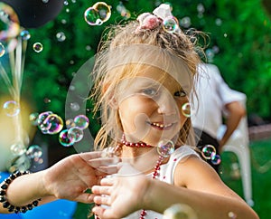 A girl dances in soap bubbles at a children's party. Children's birthday party in the backyard in the summer