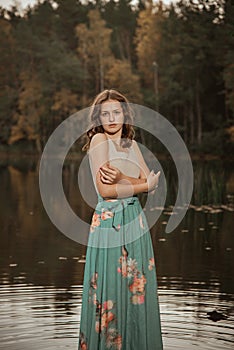 A girl is dancing on a wooden bridge against the backdrop of a forest lake.