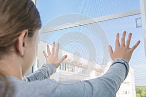 The girl dangerously put her hands on a loosely fixed mosquito net window, the danger of falling from the window, close-up