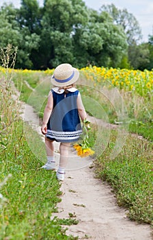 Girl in a dark blue dress near a field of blossoming sunflowers