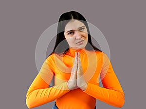 Girl with dark hair in a bright orange sweater on a gray background. implore