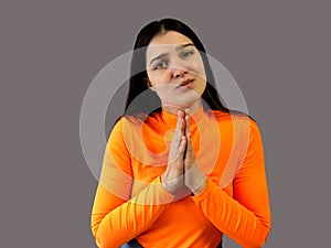 Girl with dark hair in a bright orange sweater on a gray background. implore photo