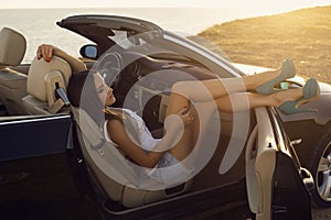 girl with dark hair posing in luxury cabriolet on sunset coast