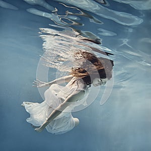 A girl with dark hair in a white dress swims underwater as if flying in zero gravity