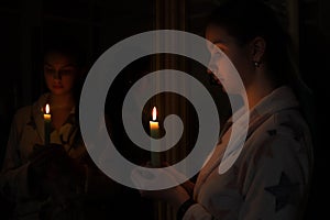 A girl in a dark room with a candle in her hand in front of a mirror with reflections