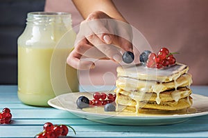 Girl decorates pancakes fresh berries. Tasty breakfast with condensed milk