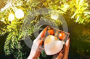 Girl is decorating christmas tree with lights. Present box with toys in woman`s hands. White fluffy heart. Love and holidays