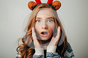 Girl with deer horns in a sweater smiles. She is shocked by the gift for the new year. Incredible discounts for